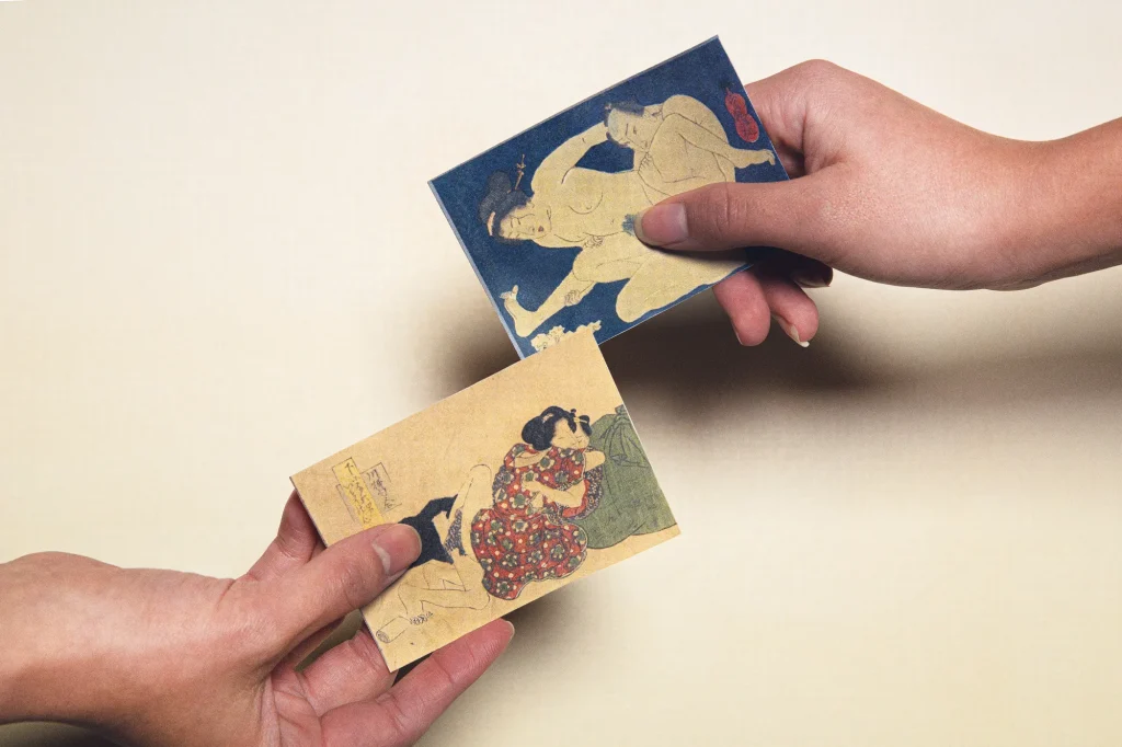 Hands holding miniature mameban shunga prints, showing the small scale of Edo period ukiyo-e works