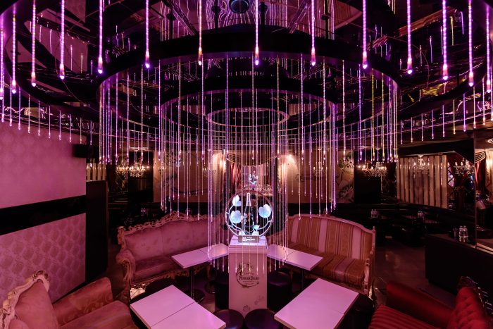 Interior of a Tokyo host club with pink lighting, chandeliers, and a champagne display.